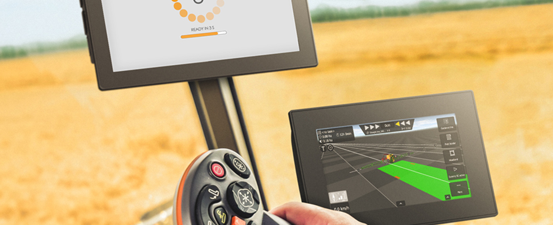 Display computer in agricultural vehicle cabin with hand on joystick