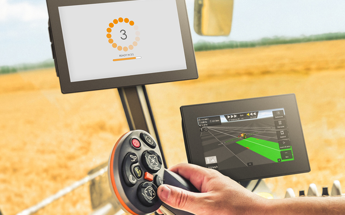 Display computer in agricultural vehicle cabin with hand on joystick