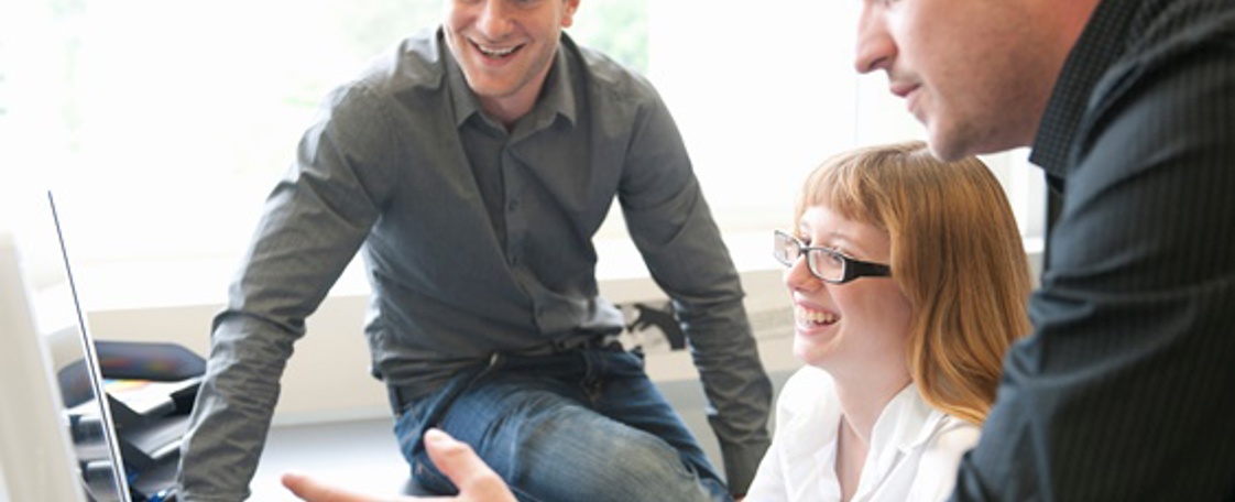 Employees looking at computer screen cooperating.