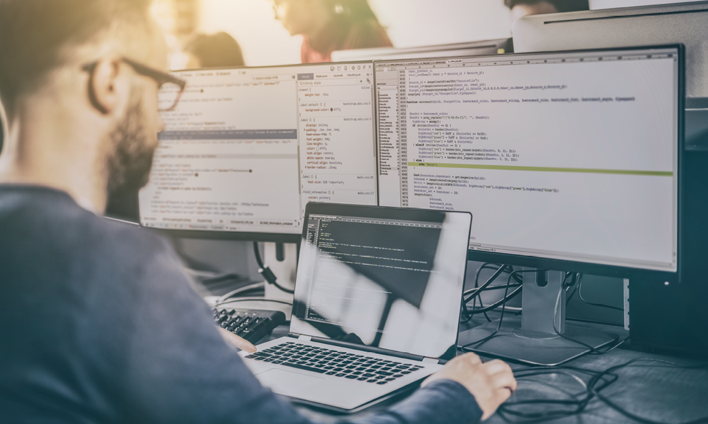 Image with employee working on computer with multiple screens