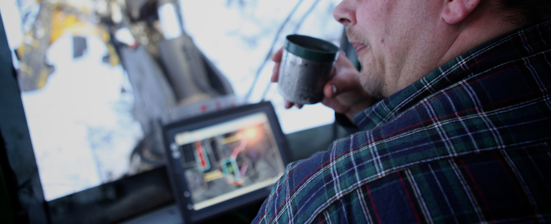 Display computer solution in forestry machine cabin with man drinking coffee.
