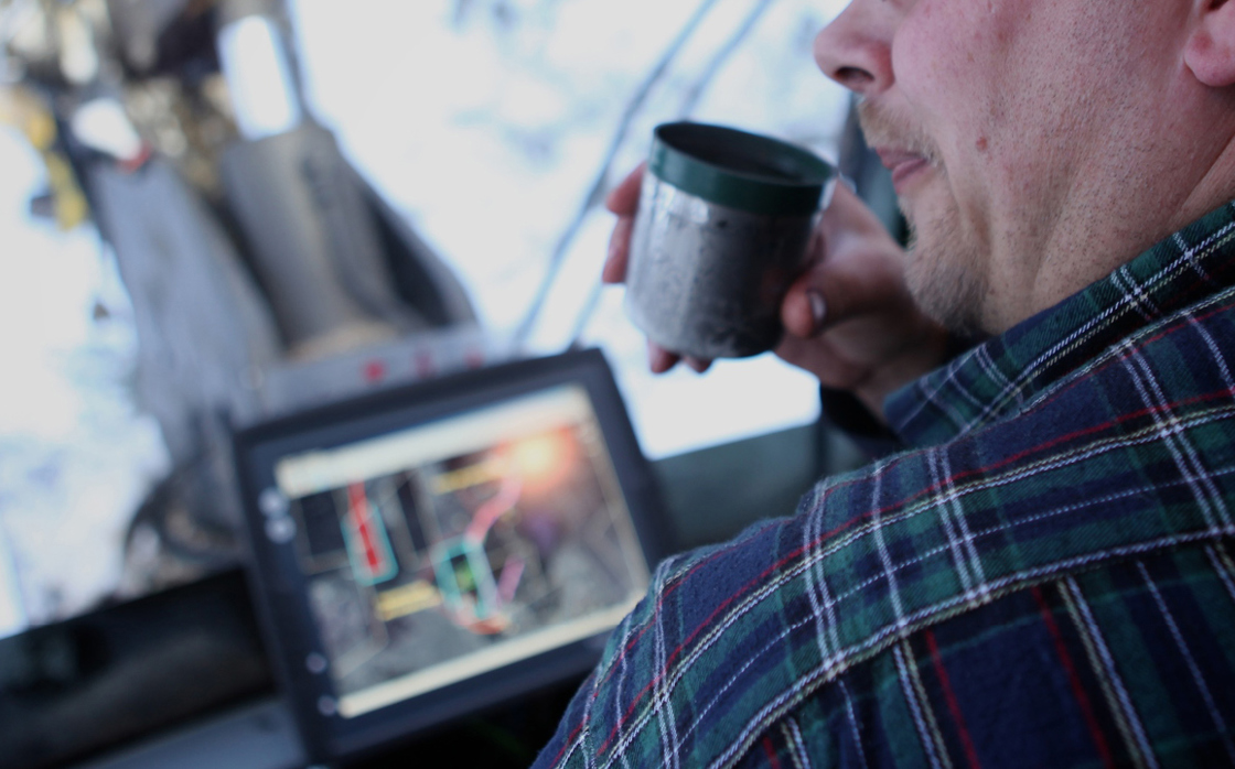 Display computer solution in forestry machine cabin with man drinking coffee.